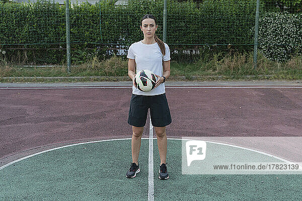 Young woman holding ball standing in soccer court