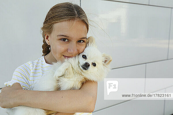 Happy girl embracing dog in front of wall