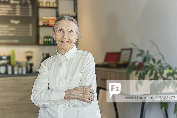 Smiling senior woman with arms crossed standing in cafe