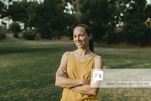 Happy woman with arms crossed standing at park