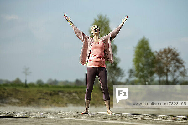 Mature woman standing with arms raised screaming on pier