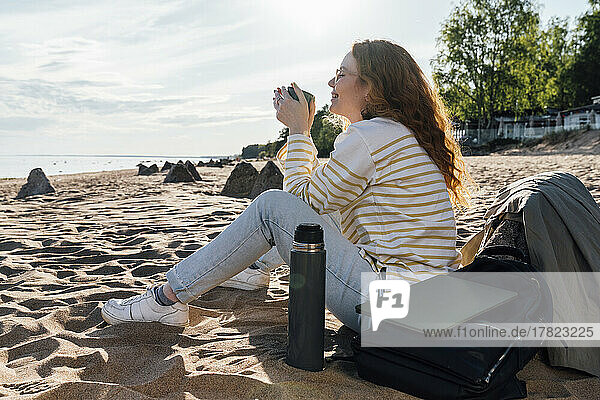 Smiling woman having coffee in insulated cup at beach