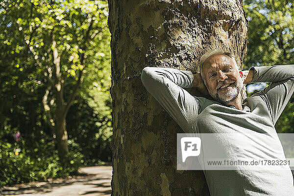 Happy man with eyes closed leaning on tree trunk