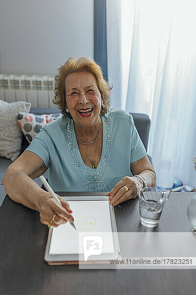Cheerful senior woman with tablet PC sitting at table
