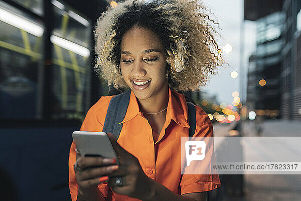 Young woman with curly hair using smart phone at night