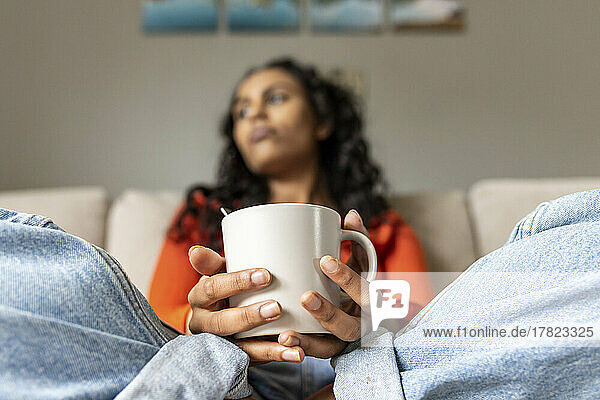 Nachdenkliche Frau mit Kaffeetasse sitzt im Wohnzimmer