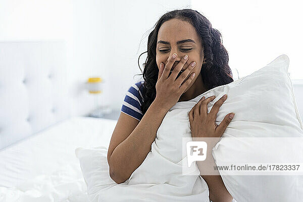 Young woman sitting and yawning on bed at home