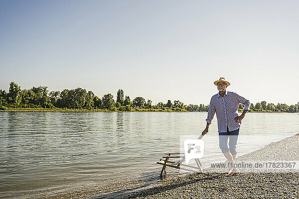 Man wearing hat standing with hand on hip at riverbank