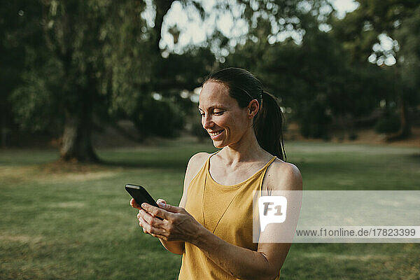 Smiling woman using phone standing at park