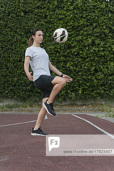 Young woman kicking soccer ball with knee in sports court