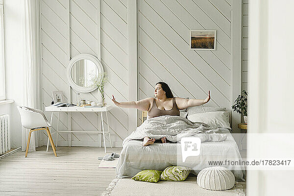 Woman with arms outstretched sitting on bed at home