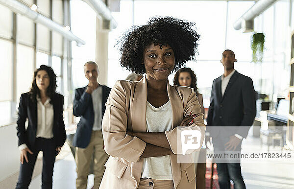 Businesswoman with arms crossed standing with colleagues at office