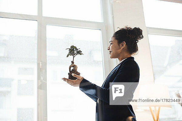 Smiling businesswoman holding plant by window in office
