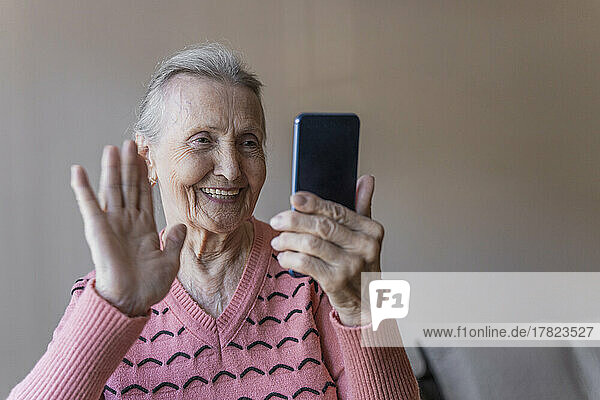 Happy woman waving on video call through smart phone at home