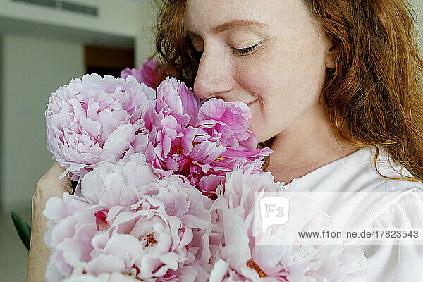 Lächelnde Frau  die zu Hause rosa Blumen riecht