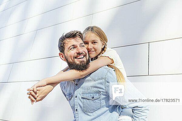 Happy man giving piggyback ride to daughter on sunny day