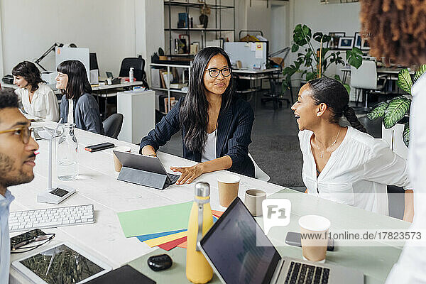 Lächelnde Geschäftsfrauen am Schreibtisch bei einer Bürobesprechung