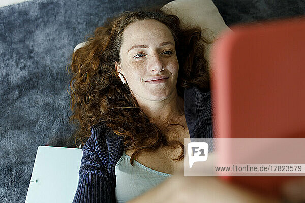 Smiling woman using phone lying on carpet at home