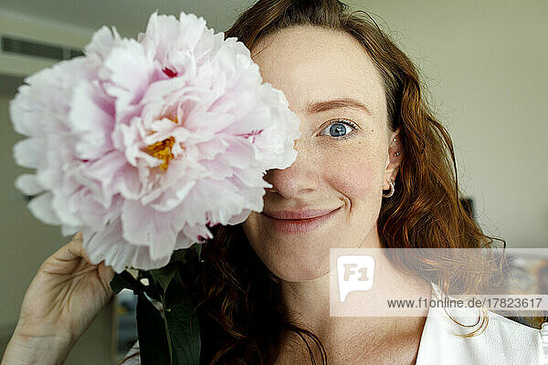 Smiling woman holding flower in front of eye