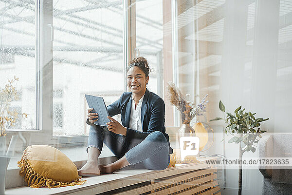 Happy young businesswoman with tablet PC sitting in front of window