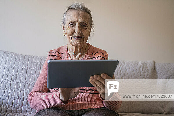 Happy senior woman using tablet PC in living room