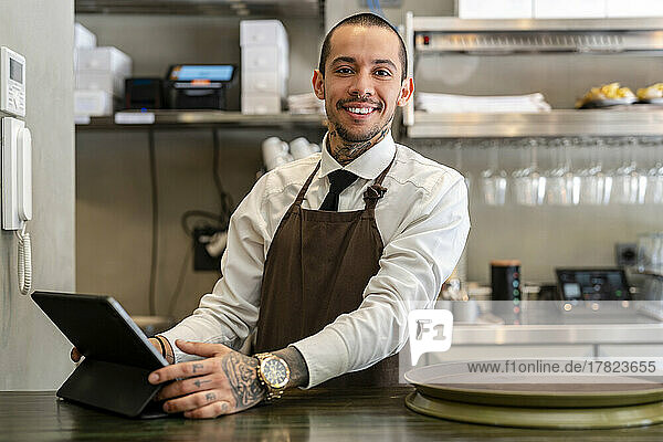 Smiling bartender with tablet PC standing at bar counter
