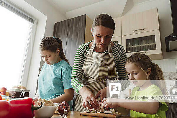 Mother helping daughter in preparing pizza at home