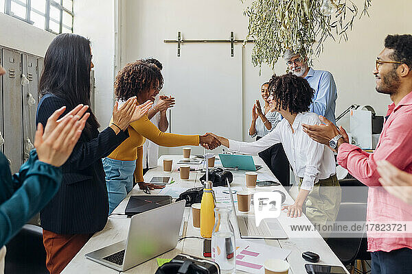 Smiling businesswomen shaking hands by colleagues in office