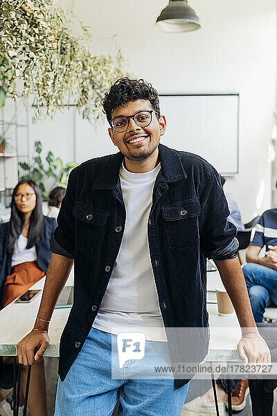 Junger lächelnder Geschäftsmann mit Brille im Coworking-Büro