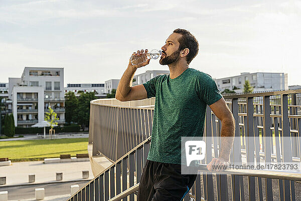 Bearded man drinking water leaning on railing