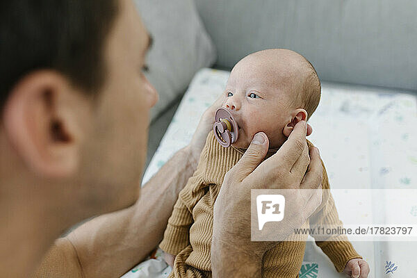Mann hält Baby mit Schnuller zu Hause