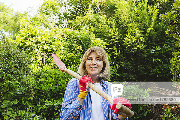 Smiling woman carrying shovel in garden