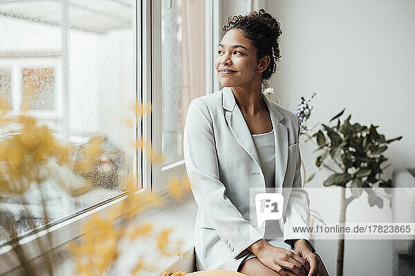 Smiling young businesswoman sitting by window at office