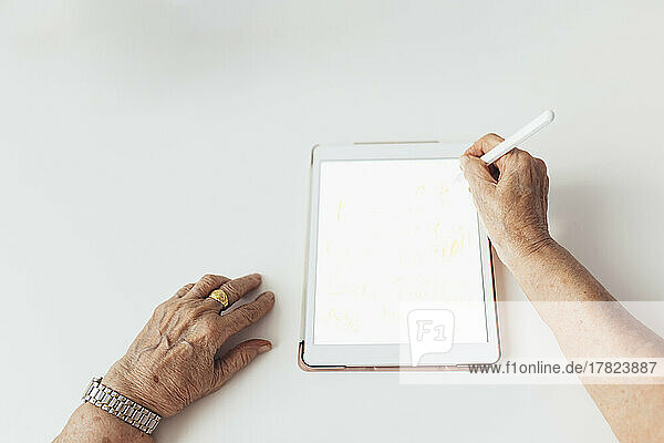 Hands of senior woman using tablet PC over white background