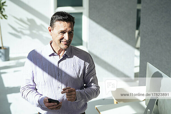 Smiling businessman holding smart phone at office