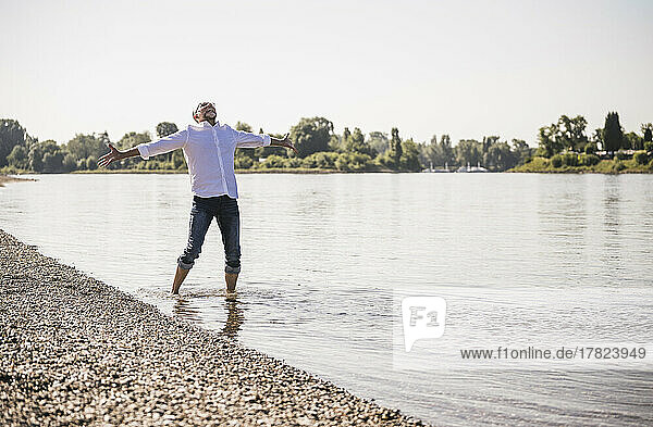Senior man standing with arms outstretched at riverbank