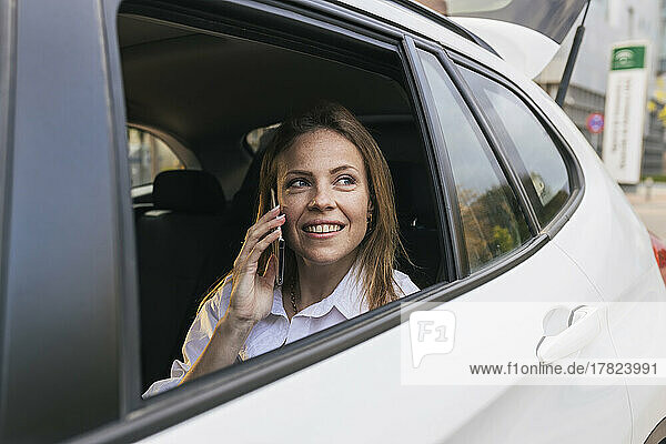 Smiling businesswoman talking on phone looking through car window