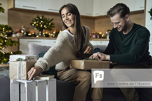 Mann verpackt Geschenkbox von Frau im Wohnzimmer zu Weihnachten