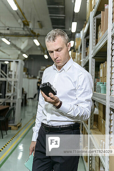 Businessman examining machine part standing by rack in warehouse