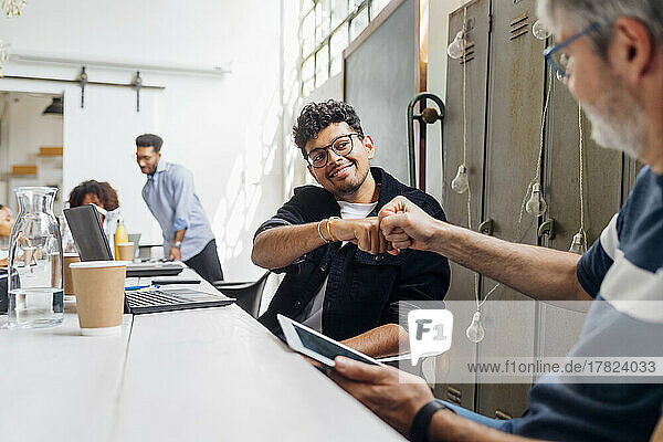 Smiling businessman giving fist bump to colleague at workplace