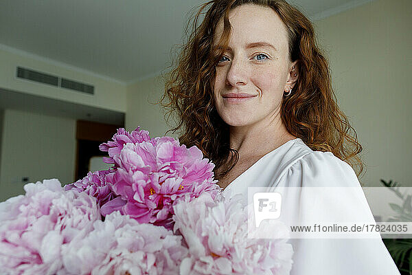 Happy redhead woman with flowers at home