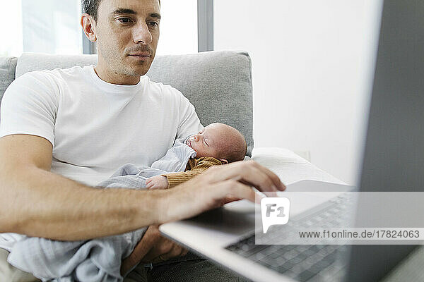 Man carrying baby in arm working from home