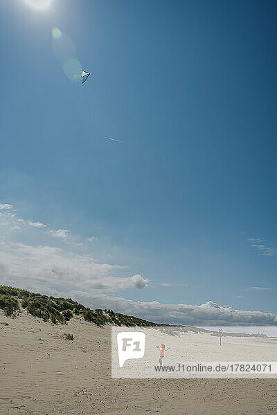 Junge lässt an einem sonnigen Tag Drachen am Strand steigen