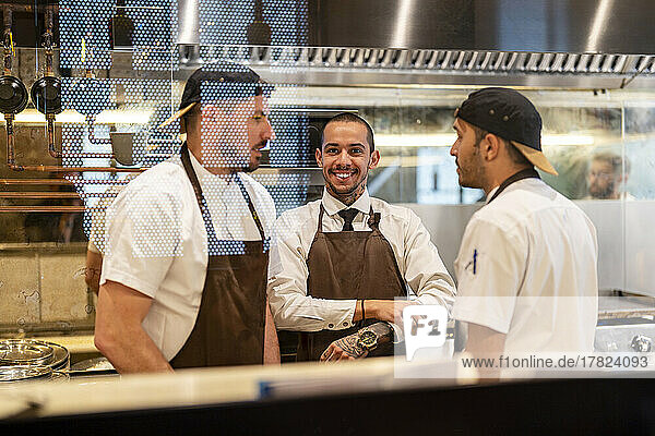 Smiling chef standing with colleagues seen through glass