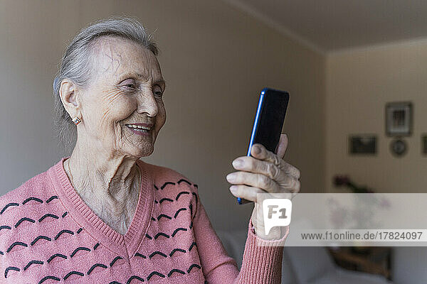 Smiling woman talking on video call through smart phone at home