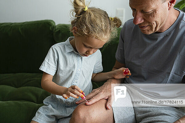 Daughter painting nails of father sitting on sofa at home