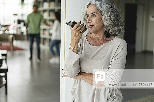 Businesswoman talking on speaker phone near column at office