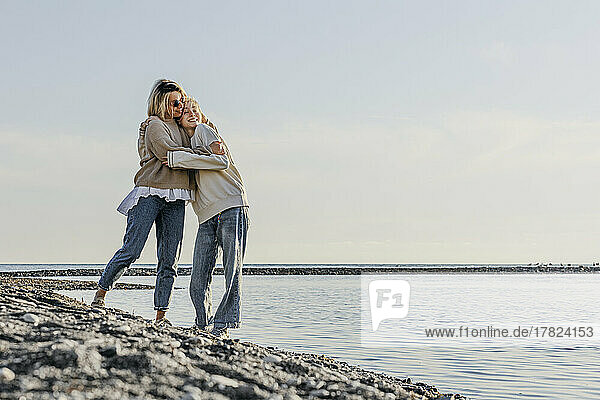 Mother hugging daughter standing by sea at beach