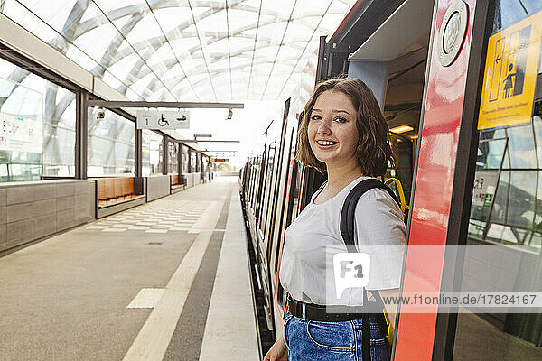 Smiling teenage girl standing at doorway of train at railroad station