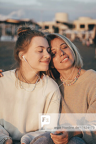 Smiling mother and daughter with eyes closed enjoying music through in-ear headphones